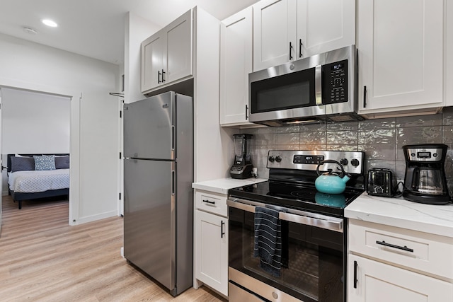 kitchen with white cabinetry, tasteful backsplash, light hardwood / wood-style flooring, stainless steel appliances, and light stone counters