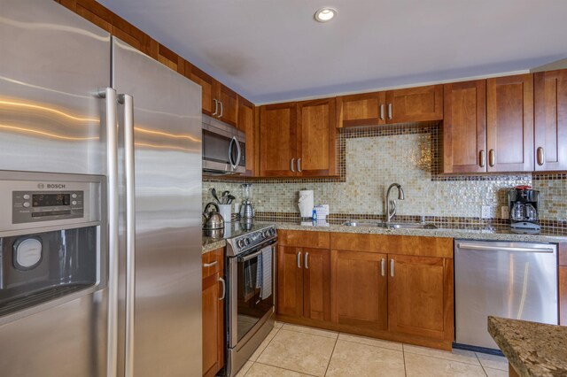 kitchen with light tile patterned floors, appliances with stainless steel finishes, backsplash, a sink, and stone countertops