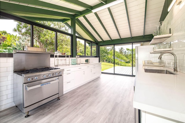 interior space with high end stainless steel range oven, white cabinetry, vaulted ceiling with beams, light hardwood / wood-style flooring, and sink