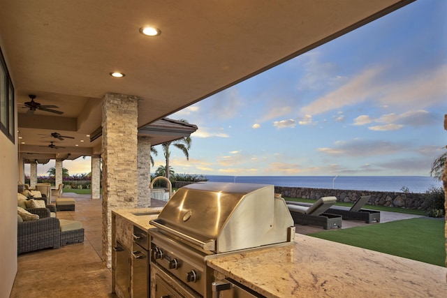 patio terrace at dusk featuring an outdoor living space, area for grilling, sink, a water view, and an outdoor kitchen