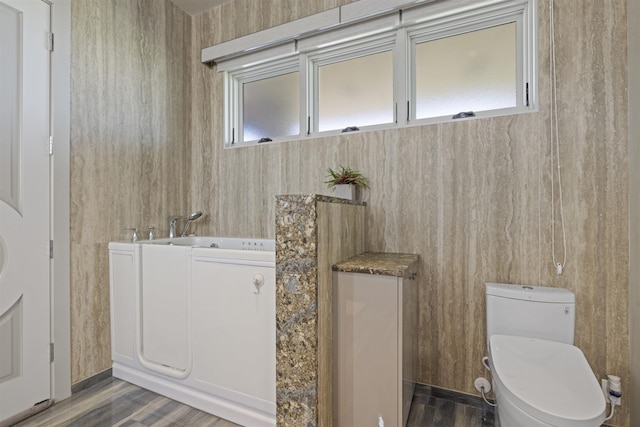 bathroom with toilet, a washtub, and hardwood / wood-style floors