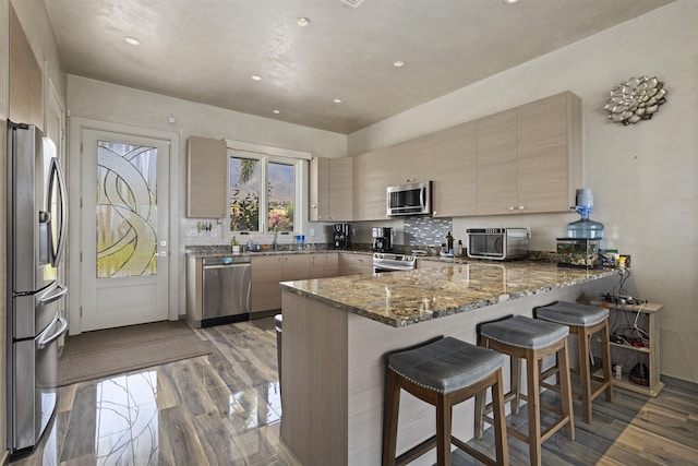 kitchen featuring kitchen peninsula, sink, a breakfast bar area, stainless steel appliances, and dark stone counters