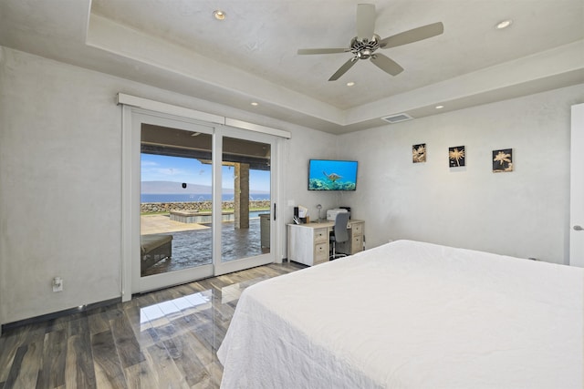 bedroom with ceiling fan, access to exterior, a tray ceiling, and dark hardwood / wood-style flooring