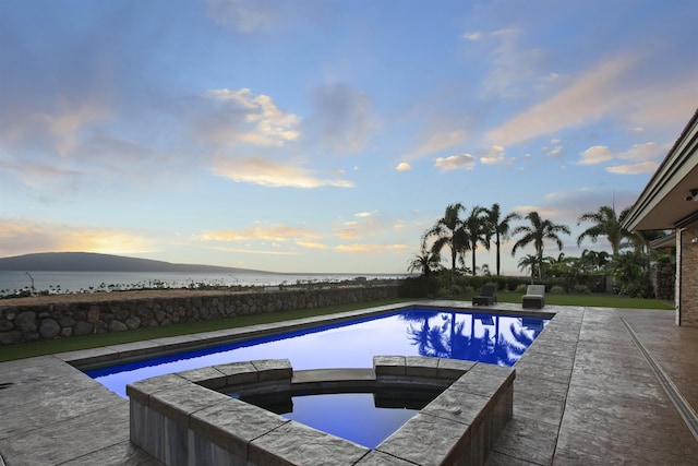 pool at dusk featuring an in ground hot tub, a water and mountain view, and a patio