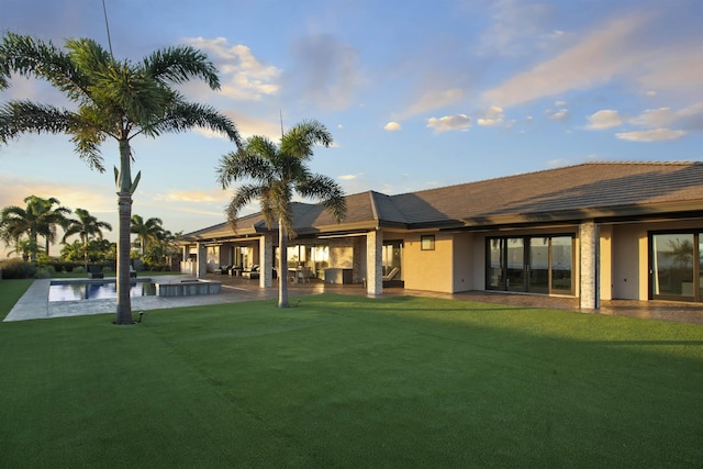 back house at dusk with a patio area and a yard