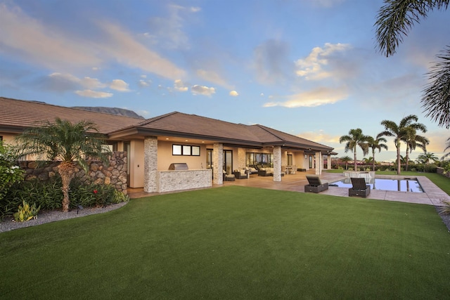 back house at dusk featuring an outdoor living space, a lawn, and a patio