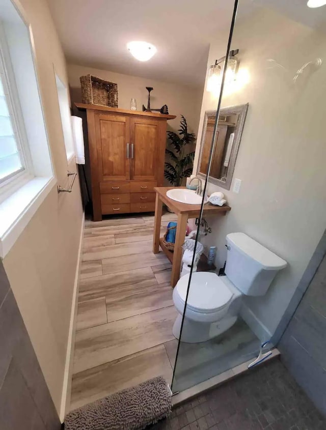 bathroom with toilet, wood finished floors, baseboards, and a sink