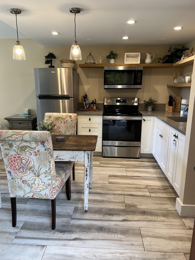 kitchen featuring light wood-style flooring, decorative light fixtures, dark countertops, white cabinetry, and appliances with stainless steel finishes