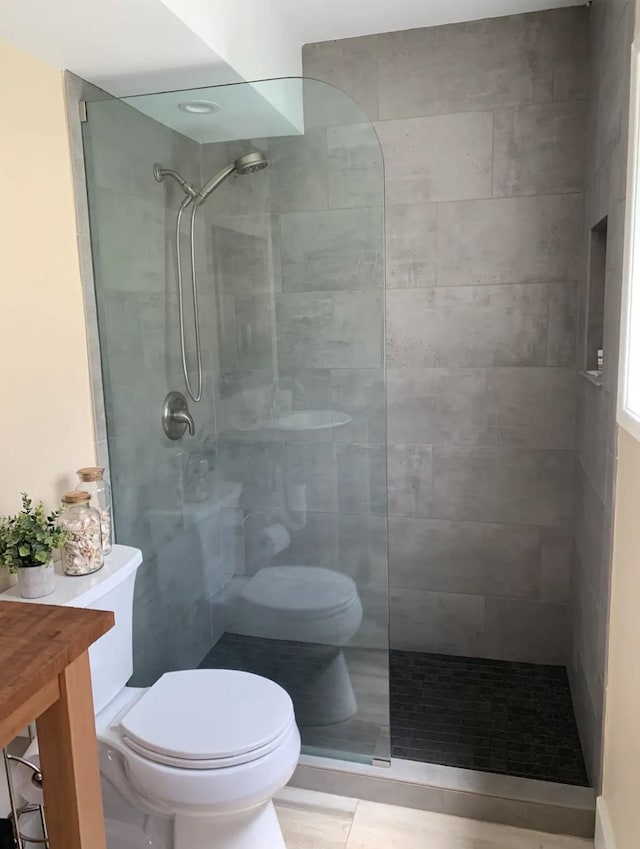 bathroom featuring a tile shower, vanity, tile patterned floors, and toilet