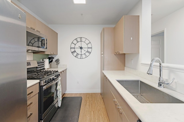 kitchen with light brown cabinetry, stainless steel appliances, light countertops, light wood finished floors, and a sink