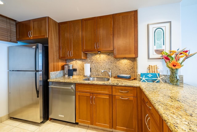 kitchen featuring light stone counters, stainless steel appliances, decorative backsplash, brown cabinetry, and a sink