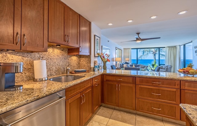 kitchen featuring tasteful backsplash, dishwasher, brown cabinets, light stone countertops, and a sink