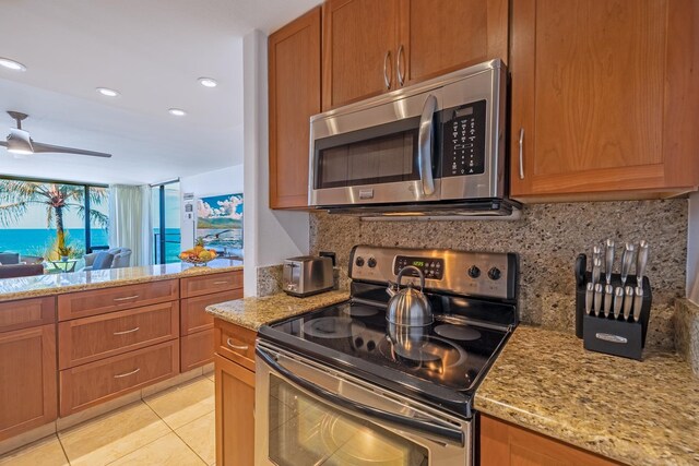 kitchen featuring light stone counters, light tile patterned flooring, appliances with stainless steel finishes, tasteful backsplash, and brown cabinetry