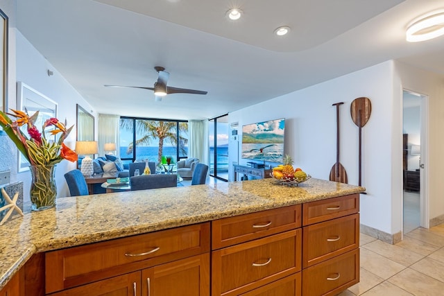 kitchen featuring light stone counters, light tile patterned floors, brown cabinetry, a ceiling fan, and open floor plan