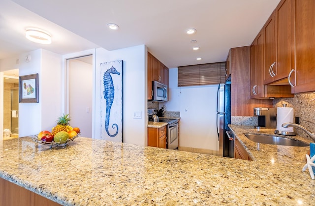 kitchen featuring brown cabinets, stainless steel appliances, tasteful backsplash, a sink, and light stone countertops