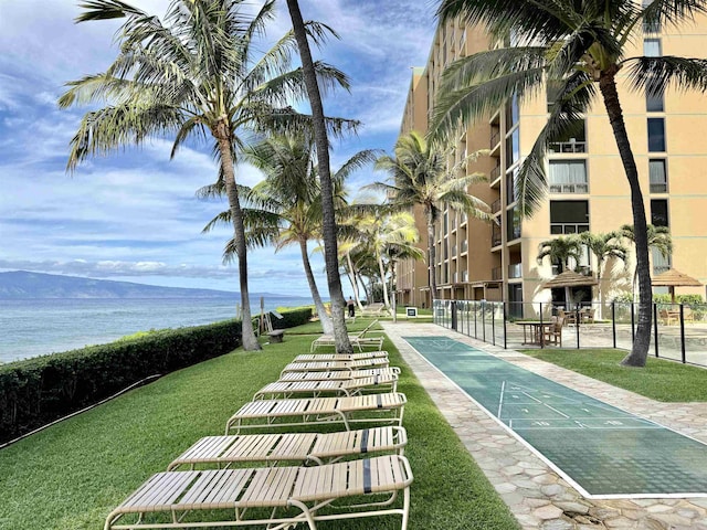 view of community with a yard, a water view, fence, and shuffleboard