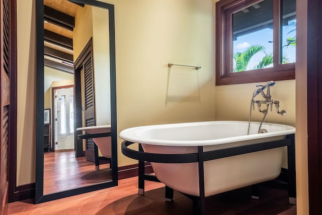 bathroom featuring a soaking tub, plenty of natural light, baseboards, and wood finished floors