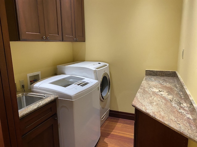 laundry room featuring washing machine and dryer, a sink, baseboards, cabinet space, and dark wood finished floors