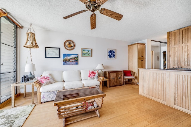 living room with ceiling fan, light wood-type flooring, and a textured ceiling