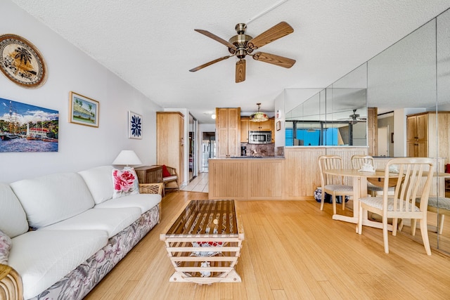 living room featuring ceiling fan, light hardwood / wood-style flooring, and a textured ceiling