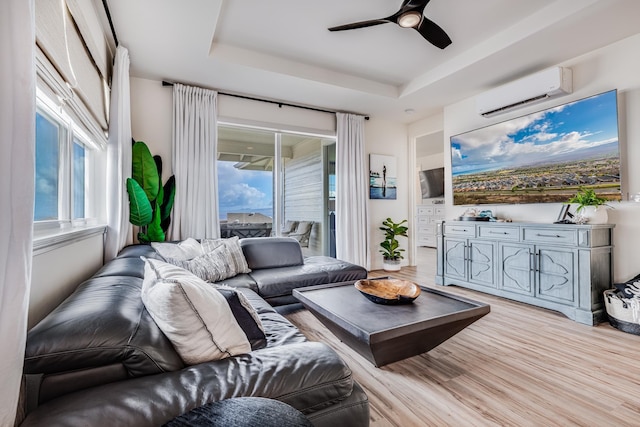 living room featuring a tray ceiling, an AC wall unit, a healthy amount of sunlight, and light hardwood / wood-style flooring