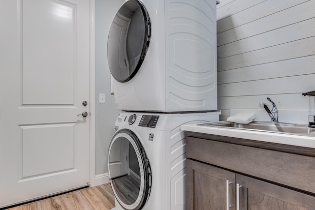 laundry area with cabinets, light hardwood / wood-style floors, stacked washer / drying machine, and sink