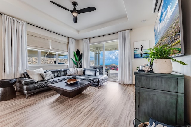 living room with a tray ceiling, ceiling fan, and light hardwood / wood-style flooring