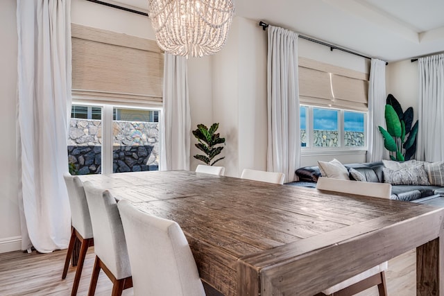 dining area with light hardwood / wood-style flooring, a healthy amount of sunlight, and an inviting chandelier