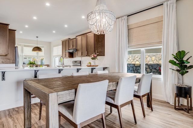 dining space with sink, an inviting chandelier, a healthy amount of sunlight, and light wood-type flooring