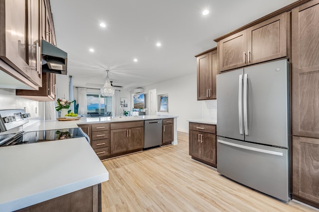 kitchen featuring kitchen peninsula, stainless steel appliances, decorative light fixtures, and light wood-type flooring