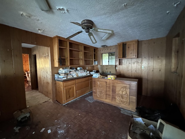 kitchen featuring open shelves, brown cabinetry, a ceiling fan, wooden walls, and a textured ceiling