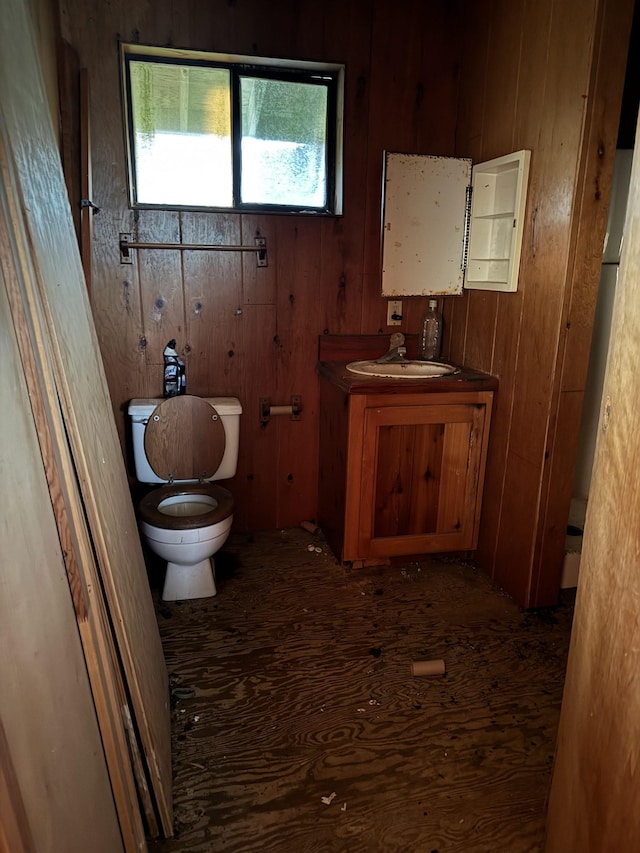 bathroom featuring toilet, wooden walls, wood finished floors, and vanity