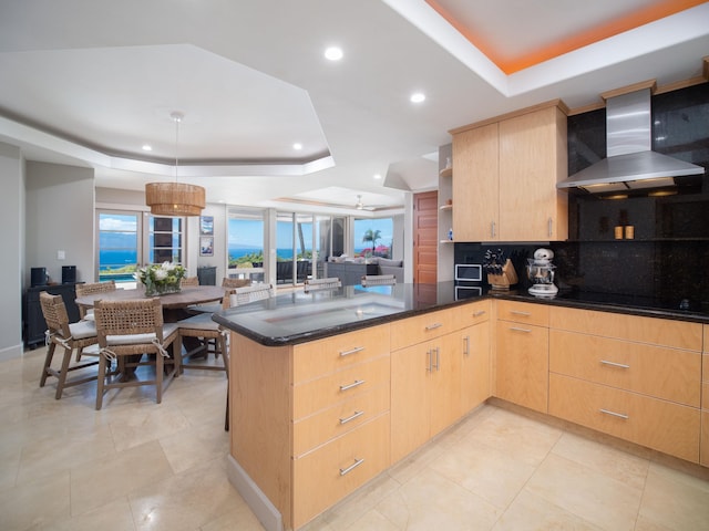 kitchen featuring tasteful backsplash, wall chimney range hood, light brown cabinets, light tile patterned floors, and a raised ceiling