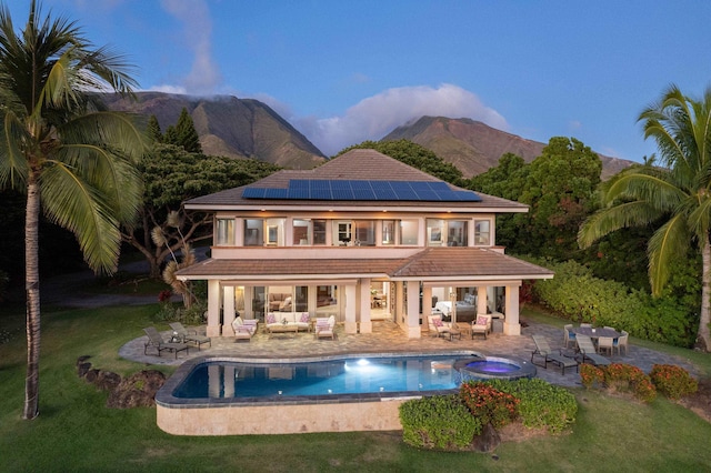 back of house featuring a patio area, a lawn, a mountain view, and solar panels