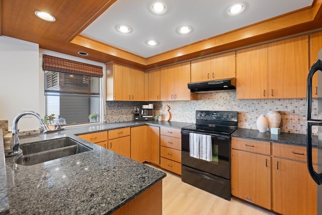 kitchen with light wood-style flooring, dark stone counters, under cabinet range hood, black / electric stove, and a sink