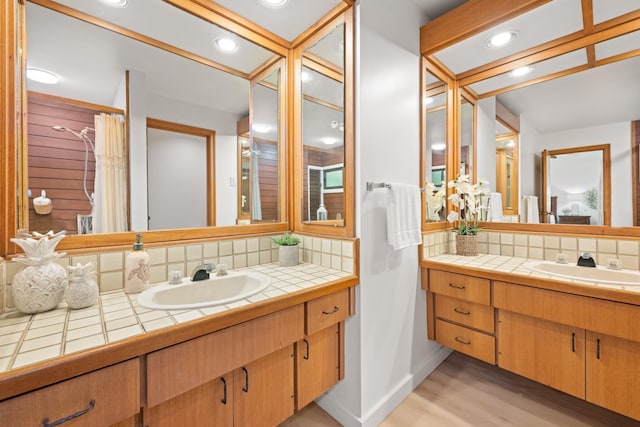 bathroom featuring wood finished floors, vanity, baseboards, and backsplash