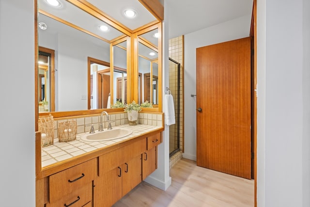 bathroom with a shower stall, vanity, decorative backsplash, baseboards, and wood finished floors