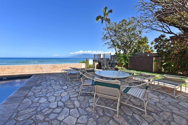 view of patio with a fenced in pool, a storage shed, and a water view