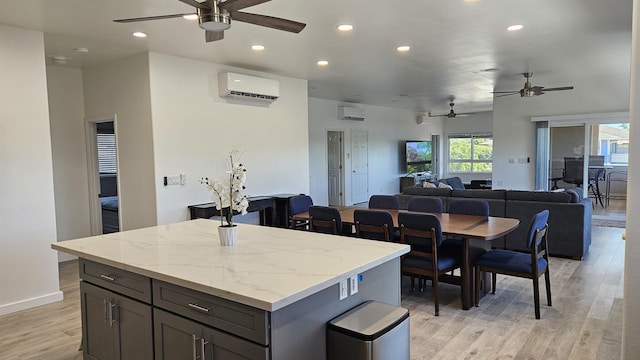 kitchen featuring an AC wall unit, light stone counters, a kitchen island, and light wood-type flooring