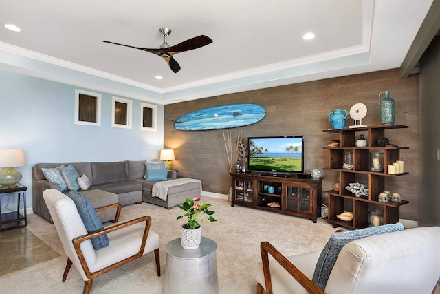 living room with a tray ceiling, wooden walls, ornamental molding, and ceiling fan