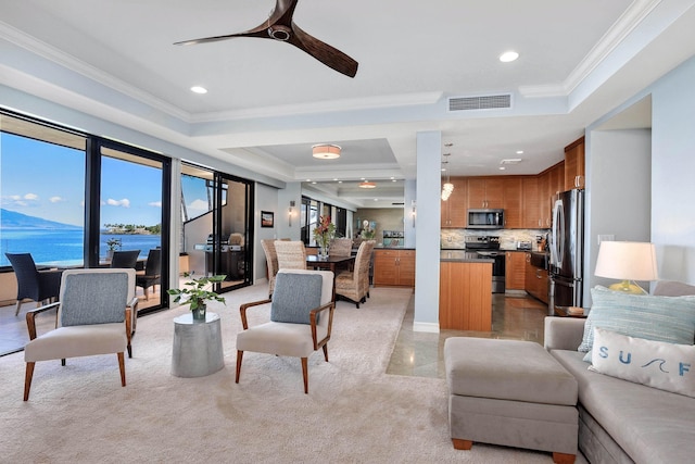 living room featuring a water view, ceiling fan, ornamental molding, and a raised ceiling