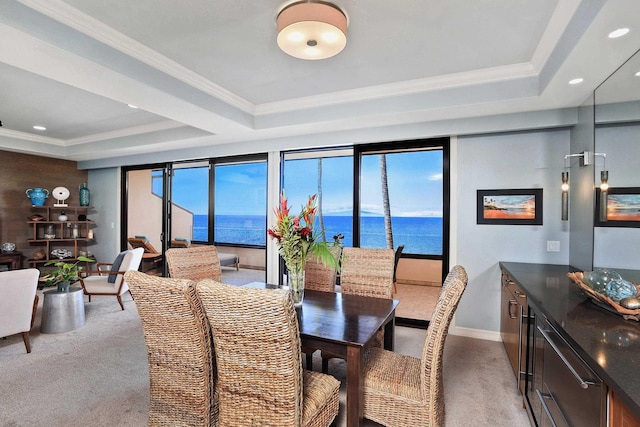 carpeted dining room featuring a water view, crown molding, and a raised ceiling