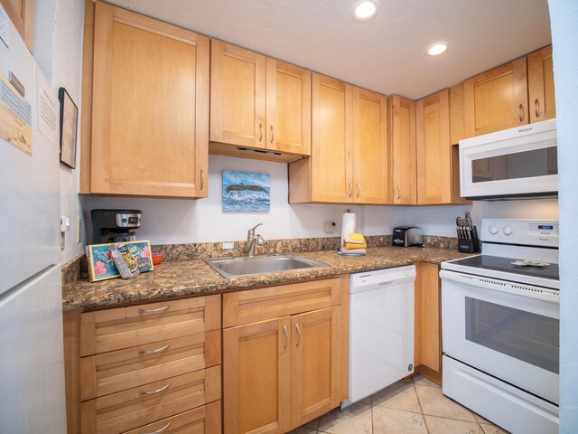 kitchen with sink, dark stone countertops, white appliances, and light tile patterned floors