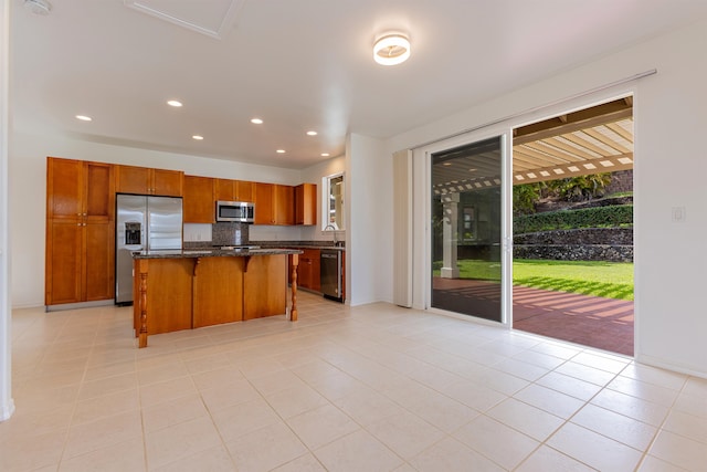 kitchen with light tile patterned floors, a kitchen breakfast bar, dark stone countertops, a kitchen island, and appliances with stainless steel finishes