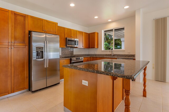 kitchen with a kitchen bar, stainless steel appliances, sink, dark stone countertops, and a kitchen island