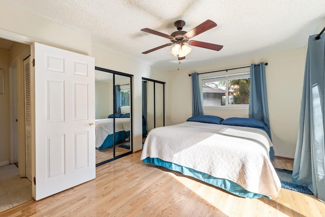 bedroom with light wood-type flooring, two closets, ceiling fan, and a textured ceiling