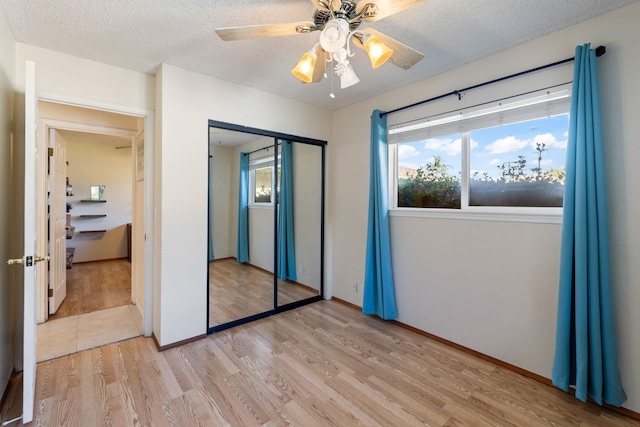 unfurnished bedroom with a textured ceiling, a ceiling fan, baseboards, light wood-style floors, and a closet