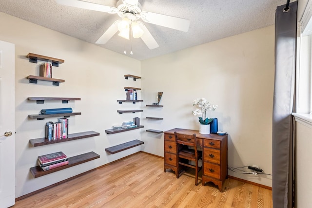 home office featuring light wood-style floors, a textured ceiling, baseboards, and a ceiling fan