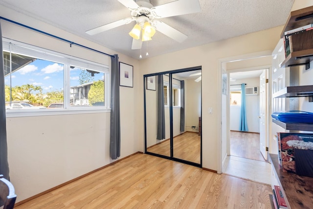 bedroom featuring a textured ceiling, light wood-style flooring, a ceiling fan, a wall mounted AC, and a closet