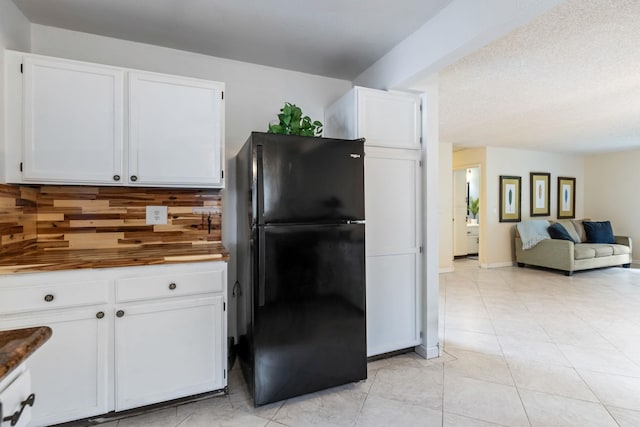 kitchen featuring light tile patterned floors, backsplash, freestanding refrigerator, open floor plan, and white cabinets